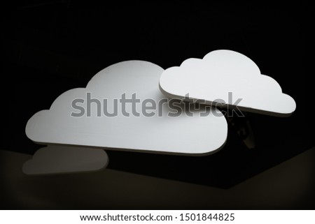 Three white wooden clouds hanging at an angle from a black ceiling design with the light hitting them used as decoration in a room