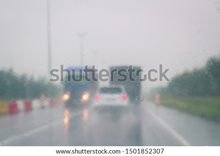 Rain on the windshield. Traffic background. Car goes on a wet asphalt road. Raindrops on the window, inside view. Truck goes towards