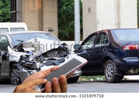 Car insurance agents take pictures of accident-damaged vehicles with a smartphone as a proof of insurance claim.