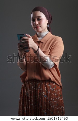 Portrait of beautiful young asian muslim woman taking selfie picture using mobile phone while standing isolated on grey background.