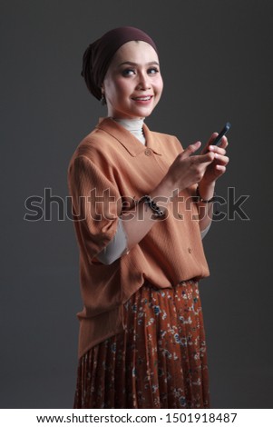 Portrait of beautiful young asian muslim woman using mobile phone while standing isolated on grey background.