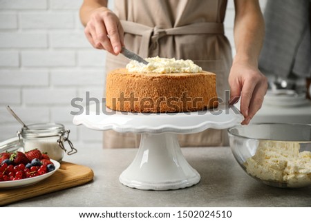 Woman decorating delicious cake with fresh cream at table indoors, closeup. Homemade pastry