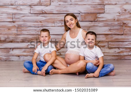 smiling pregnant woman with two children sitting on the floor on a wooden background in the Studio
