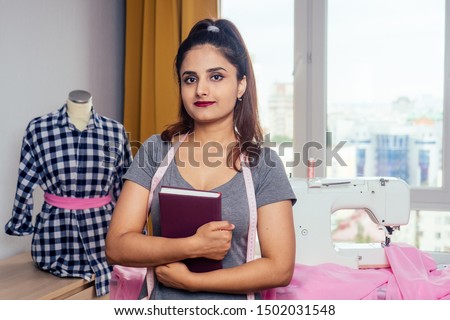 Close-up portrait of young indian seamstress sews on sewing machine in her own home studio workplace.