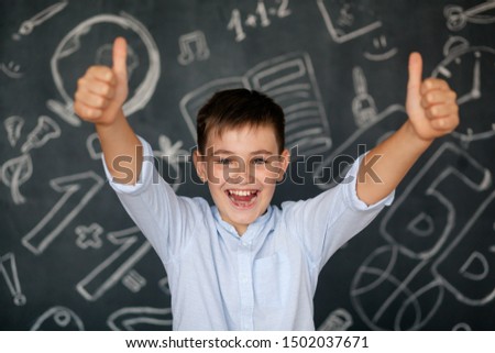 Cute happy brunette boy a schoolboy of 10-11 years old with a dazzling smile on the background of the school blackboard. Baby in a blue shirt.