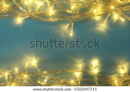Glowing Christmas lights on blue background, top view. Space for text