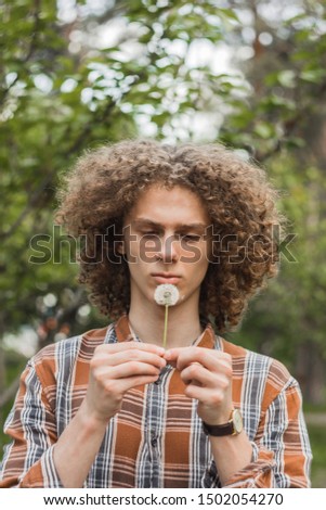 portrait of a young curly-haired guy in a summer park on the street. student and young traveler concept.