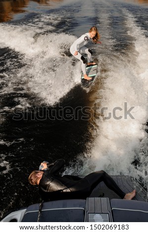 Photographer taking pictures with a camera in waterproof cover lying on the motorboat of the girl riding on the wake surf