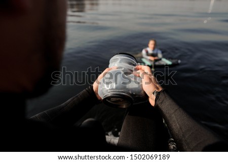 Male photographer taking pictures with a camera in waterproof cover from the motorboat of the girl on the wake surf