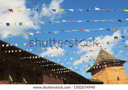 multicolored flags on blue sky background and white clouds, within the walls of a medieval castle.  pink, yellow, red, white, blue, green