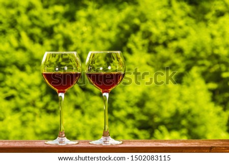 Two glasses of red wine on the deck of a wooden house on a green fresh forest background. Copyspace. Royalty-Free Stock Photo #1502083115