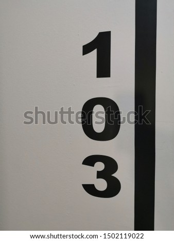 closeup of room number 103 numeral one hundred and three in black on white textured wall