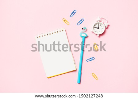 Notepad with colored pen, paper clips and alarm clock on a pink background. School, workspace, deadline concept. Flat lay, top view