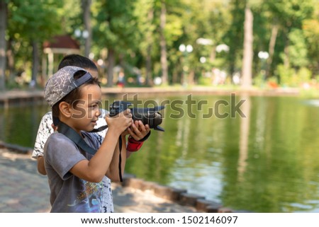 Two boys stand by the lake and take pictures of nature in the park.  Big brother teaches younger brother to take pictures