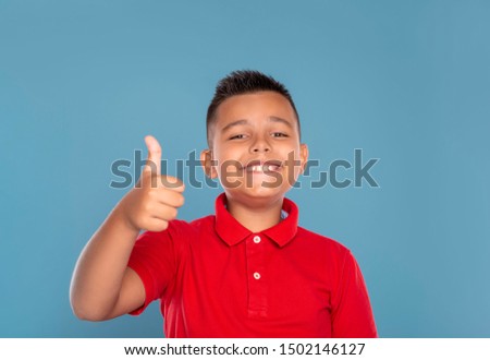 Studio shot of a young smiling boy wearing red shirt  giving you an approving gesture, isolated on blue background with copy space