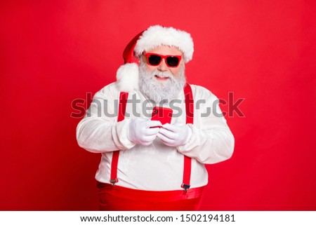Portrait of funny funky fat overweight santa claus with big abdomen belly use cell phone comment newyear posts wearing stylish trendy  eyewear eyeglasses hat reading news isolated over red background
