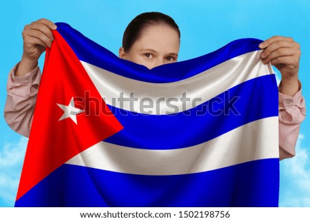 young girl holding in both hands a colored national flag on beautiful shiny silk against a blue sky, state concept, travel, immigration, horizontal, close-up, copy space