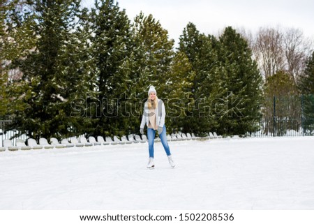 full length portrait of happy young blond woman skating at outdoor rink