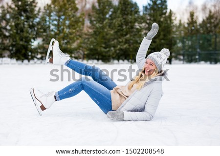 funny girl falling down while ice skating at winter rink