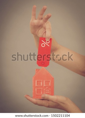 Buying house in affordable price. Hand holding small red home model and sale percentage sign. Reduced housing prices. Fall and crisis of real estate market. Low rent