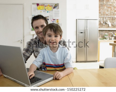 Portrait of happy son and father with laptop sitting at table in house