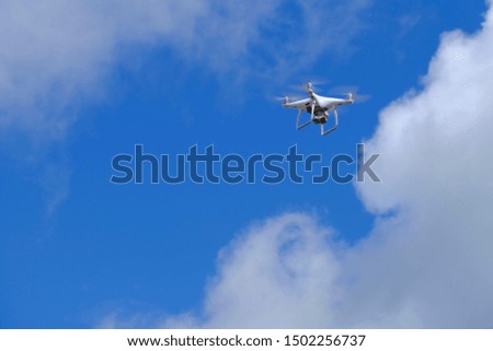 White drone quadcopter flying on the air for take a photo and video with white cloudy and blue sky background.