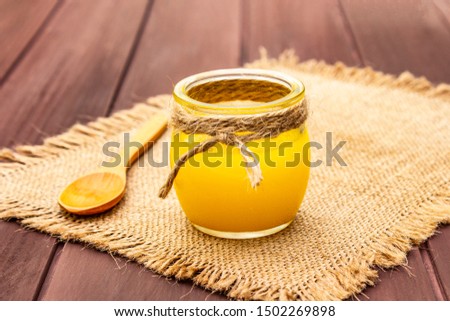 Pure or desi ghee (ghi), clarified melted butter. Healthy fats bulletproof diet concept or paleo style plan. Glass jar, wooden spoon on vintage sackcloth. Wooden boards background, copy space close up Royalty-Free Stock Photo #1502269898