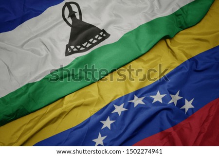 waving colorful flag of venezuela and national flag of lesotho. macro