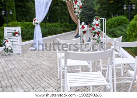 Beautiful outdoor wedding decorations, arch decorated with red and white flowers, chairs, lanterns.