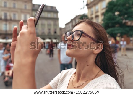 Close up portrait, young beautiful brunette girl in glasses making selfie in the center of the old city, street photo