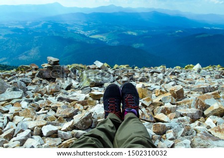 Man's legs in tracking sneakers on top of the mountain against the backdrop of mountain ranges and blue sky