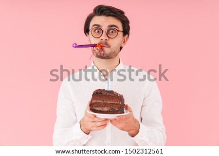 Image of caucasian surprised man wearing eyeglasses holding chocolate cake with candle isolated over pink background