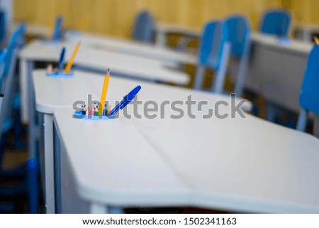 Classroom interior in junior high school. White desks are arranged in a row. Blue chairs. 