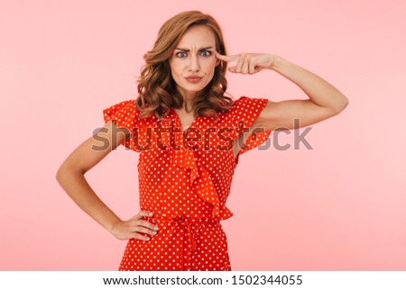 Image of displeased young woman posing isolated over pink wall background showing finger crazy gesture near head.
