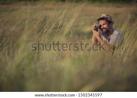 Hipster photographer taking photographs in the grass field on a sunny summer day, wearing a stray hat and grey t-shirt, joy and happiness concept 