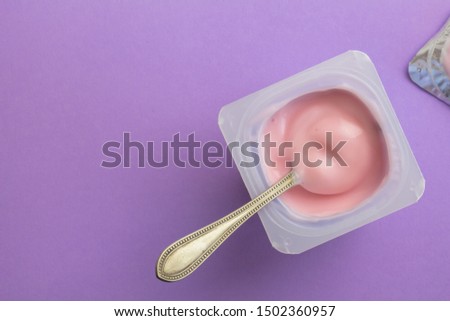 Yogurt in plastic cup with spoon - Top view of pink strawberry flavoured yoghurt on lilac background