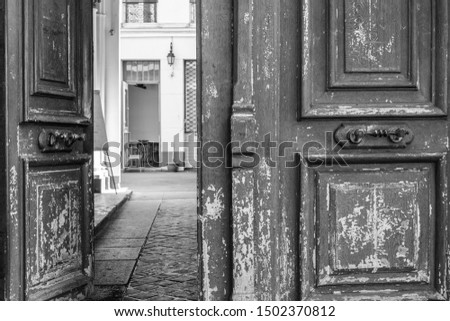 Black and white photo of shabby double door surface with peeling paint. Opened door to patio inside old house in Paris France. Vintage framed wooden door details. City life scene. Travel Europe. 