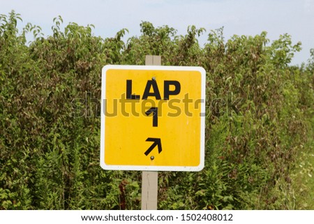 A close view of the bright yellow lap one sign in the tall grass of the field.