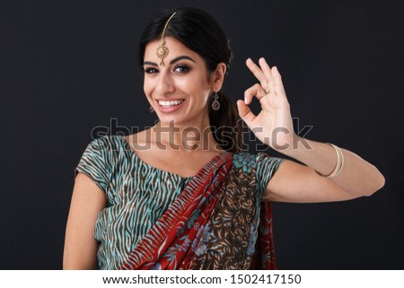 Image of pretty hindus girl wearing traditional indian costume or saree dress and ethnic jewelry showing ok sign isolated over black background