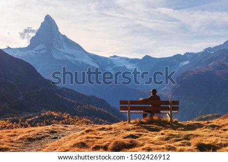 Picturesque view of Matterhorn peak and tourist sitting on wooden bench in Swiss Alps. Zermatt resort location, Switzerland. Landscape photography