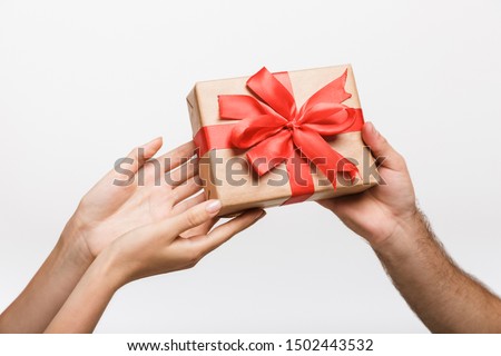 Closeup picture of a man's and woman's hands isolated over white wall background holding present surprise box.