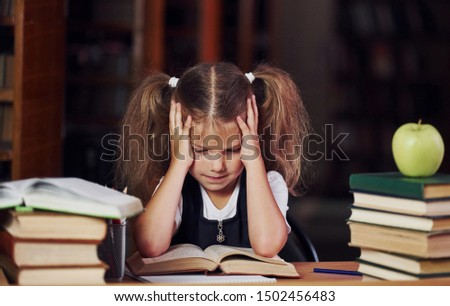 Tired of reading. Cute little girl with pigtails is in the library. Apple on the books.