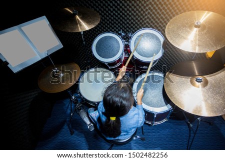 Blurry drum set and Asian girl learning and play it with wooden drumsticks in music room. The concept of musical instrument, Top view to drum player.