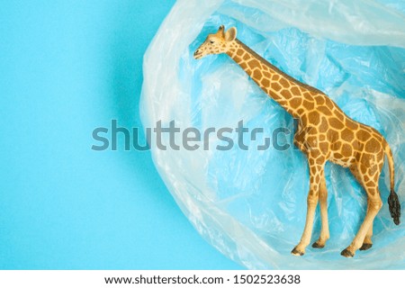 Concept for plastic pollution, environmental pollution, ecology problem. The figurine of a giraffe in a polyethylene bag. Children's toy. Flat lay, top view