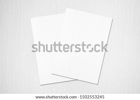 Two empty white rectangle poster or card mockups lying diagonally on top of each other with soft shadows on neutral light grey textured background. Flat lay, top view