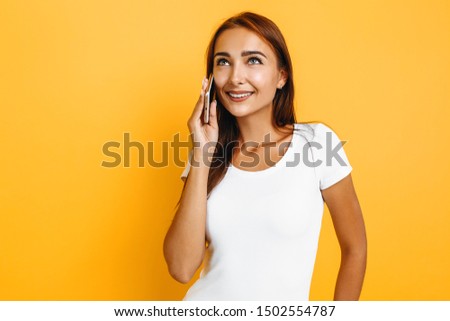 Image of a beautiful happy young girl talking on a mobile phone and smiling, on a yellow background