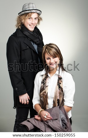image of a caucasian brother and sister dressed stylishly in winter wear smiling brightly at the camera with the gray background reflecting light and shadows
