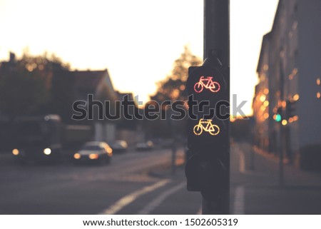 traffic light for a cycling lane showing red and yellow bicycle symbol at an intersection in dark early morning light - blurred background with cars - urban commuting concept