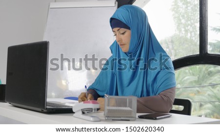 beautiful saudi business woman in hijab working in office using laptop and smartphone, copy space