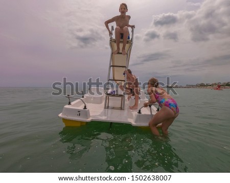 Children play on deck of plastic beach catamaran. At stern of ship is children's slide. Two boys jump in Adriatic Sea near town of Lignano Sabbiadoro Italy. Kids swim